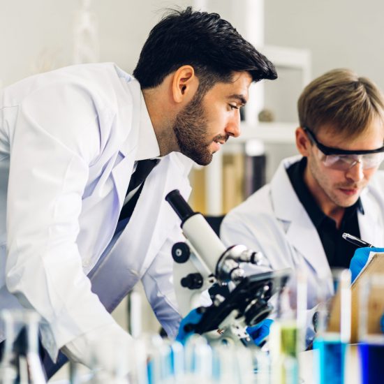 Professional two scientist man research and working doing a chemical experiment while making analyzing and mixing  liquid in test tube.Young science man dropping sample chemical on glass at laboratory